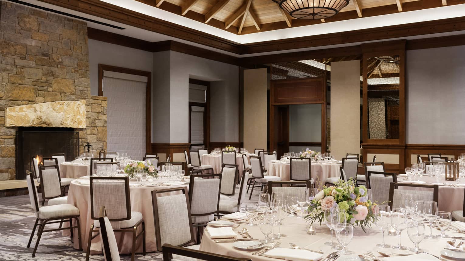 A large room with wood details, round tables with table cloths and grey chairs.