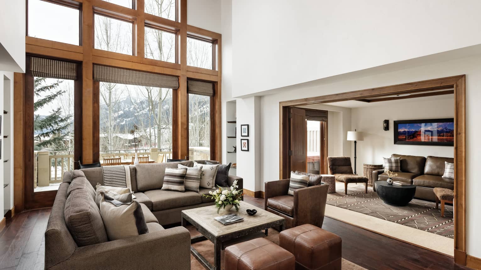 Spacious living room with high ceilings, large windows overlooking a snowy forest, sectional sofa, leather chairs and a connected seating area 