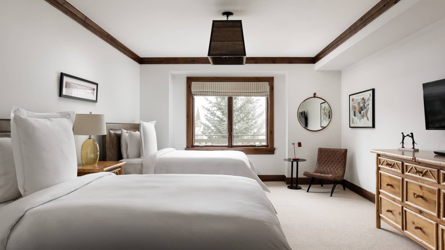 Bedroom with two beds, nightstand with lamp, rustic wooden dresser, and a reading chair by the window