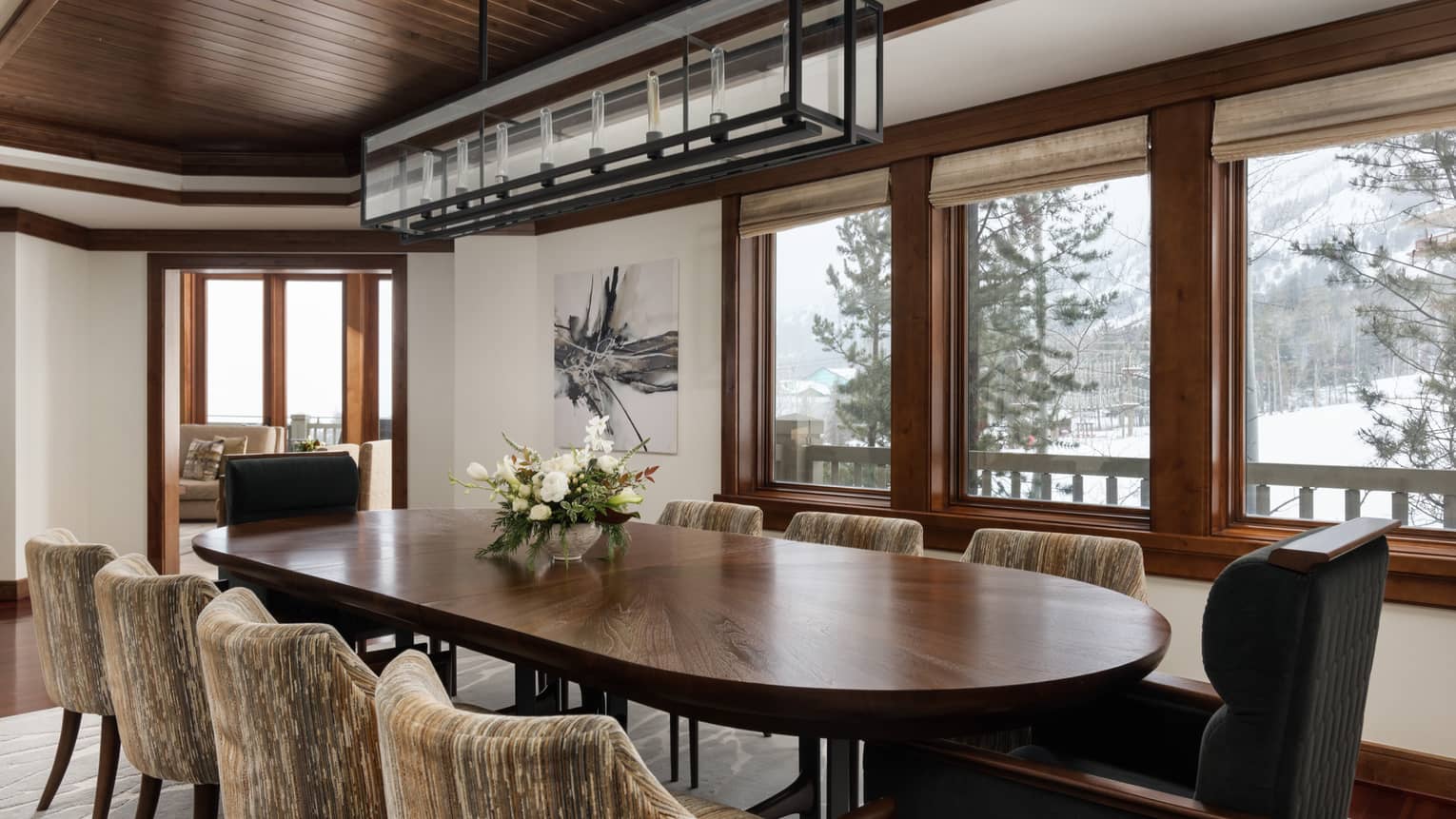 Dining room with a large dark wooden table, upholstered chairs, floral centrepiece, rectangular chandelier and snowy mountain view