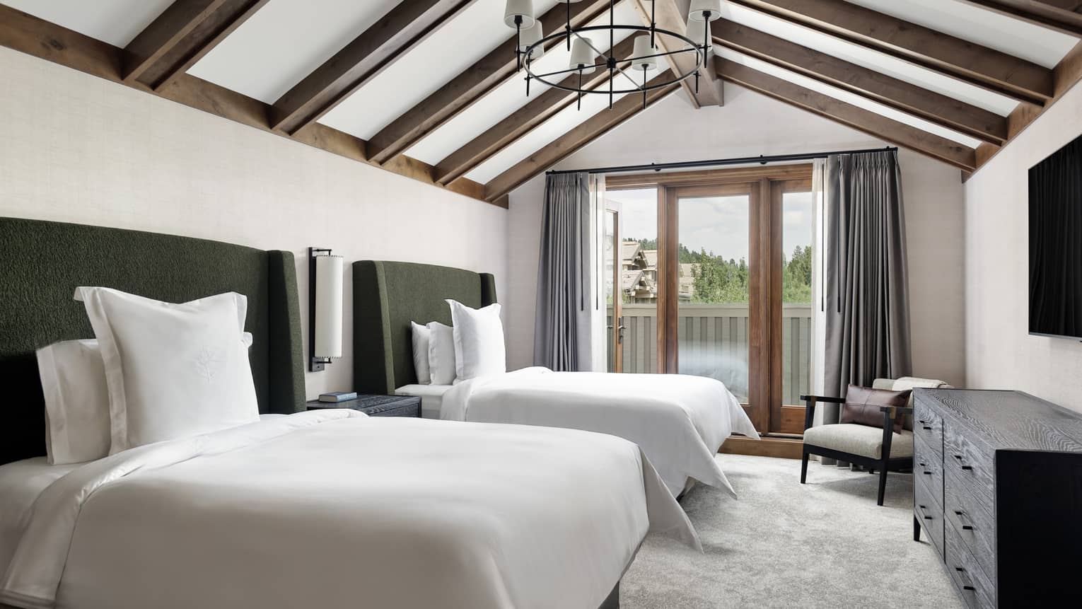 Luxury resort bedroom with two beds, dresser, armchair, vaulted ceiling with wooden beams, and walk-out balcony 