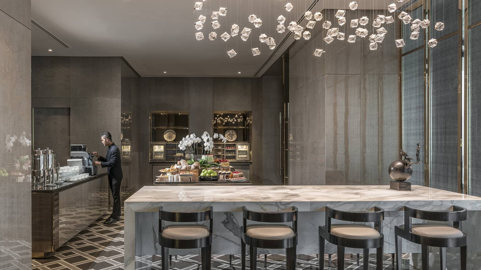 Man makes espresso coffee at counter near long white marble counter under modern lights