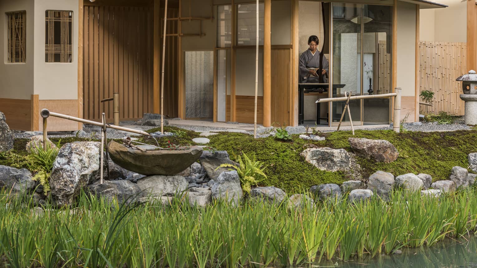 Rock garden, fountain in front of Shakusui tei building, woman in robe behind window