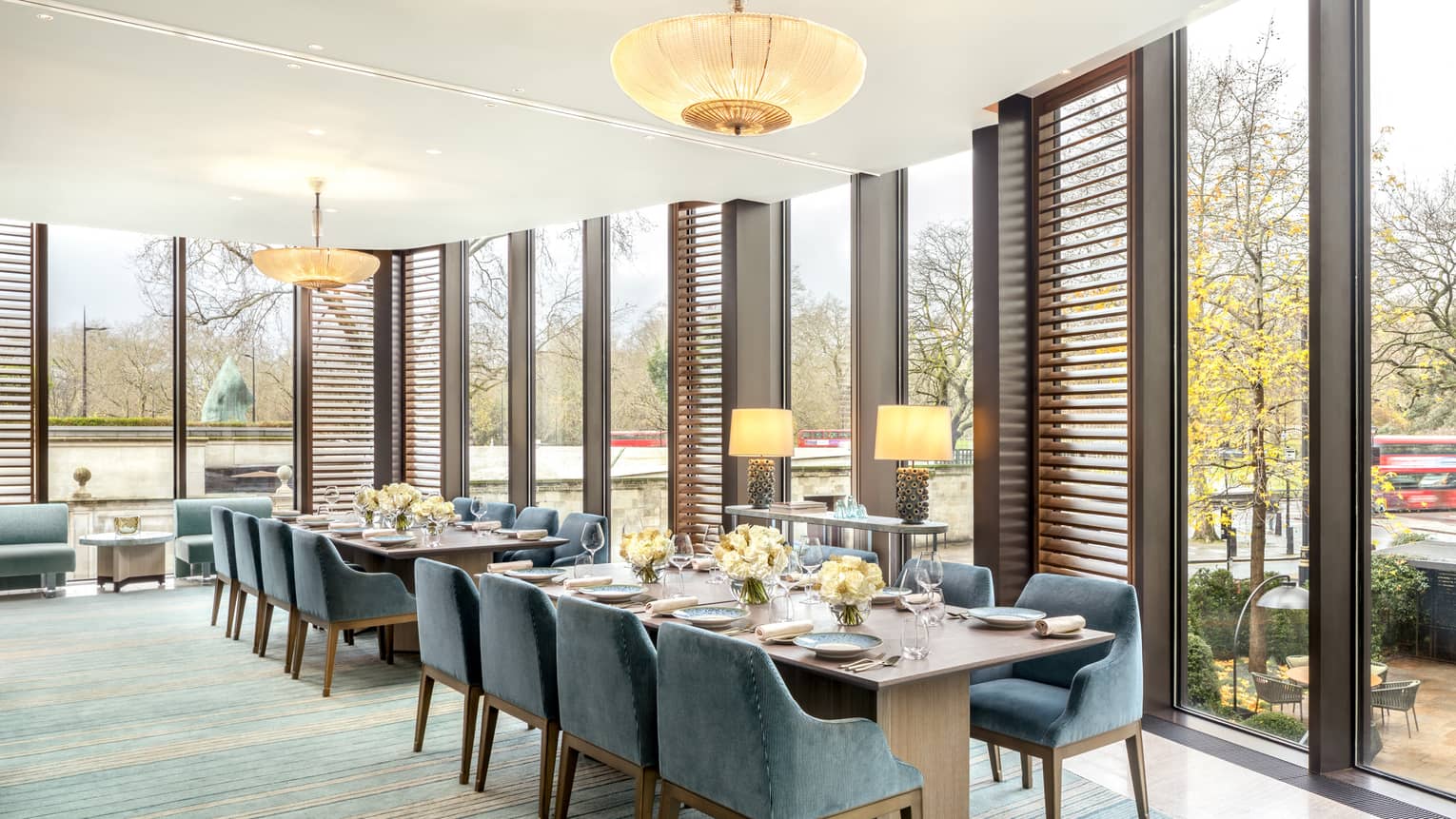 Two rectangular dining tables flanked with blue suede?covered chairs, set for a meal
