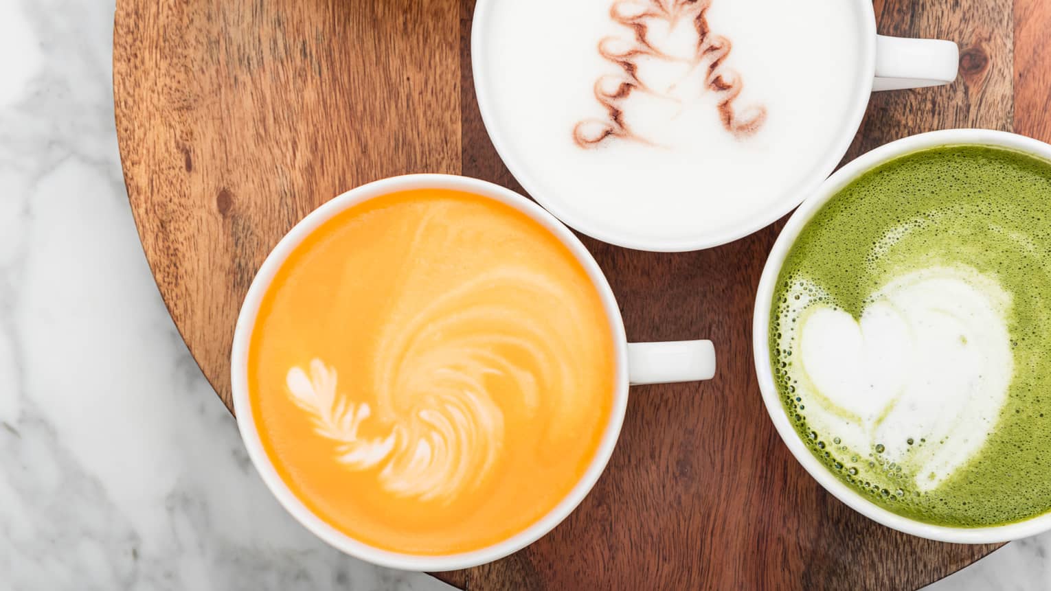 Aerial view of cups of three creamy milk, turmeric and matcha lattes