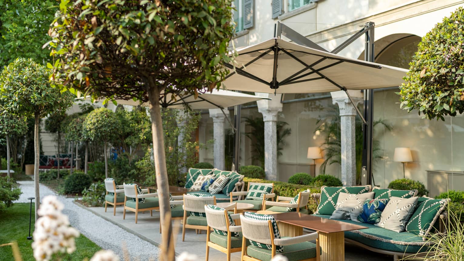 An outdoor seating area with umbrellas and green chairs surrounded by small trees.