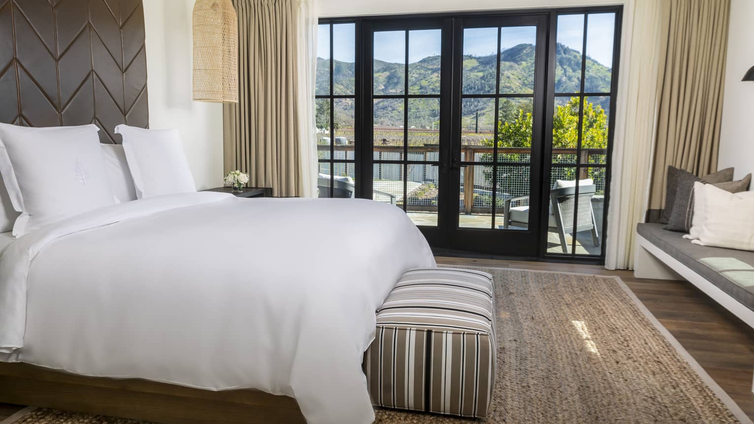 Bedroom with king bed, wooden accent wall, striped bench and walk-out terrace