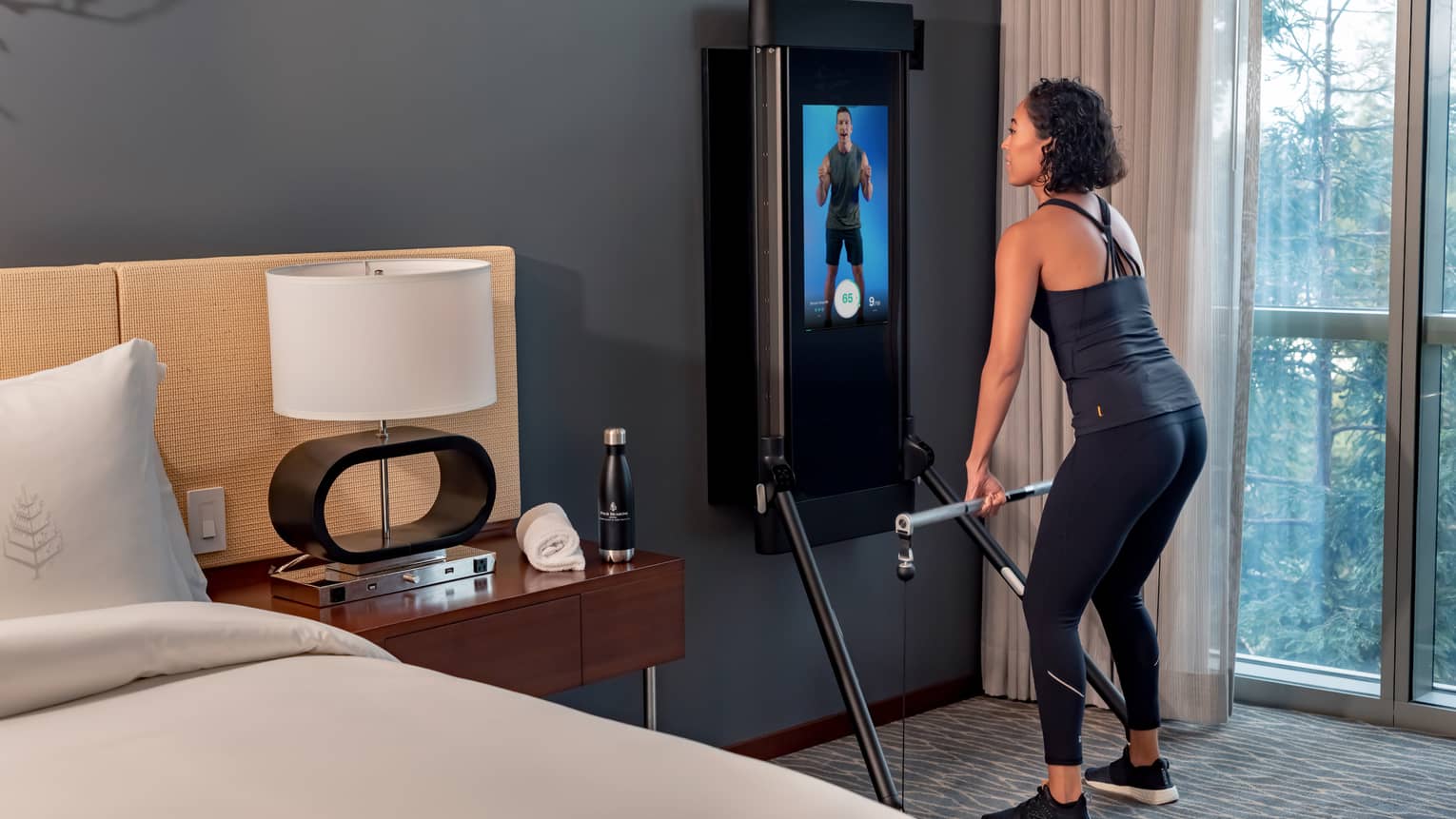 Woman exercises in front of an instructor on a screen in a Tonal technology-equipped guest room
