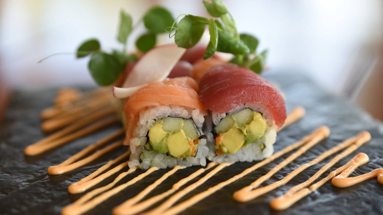 Sushi stuffed with avocado and cucumber, topped with salmon and tuna, and drizzled with sauce