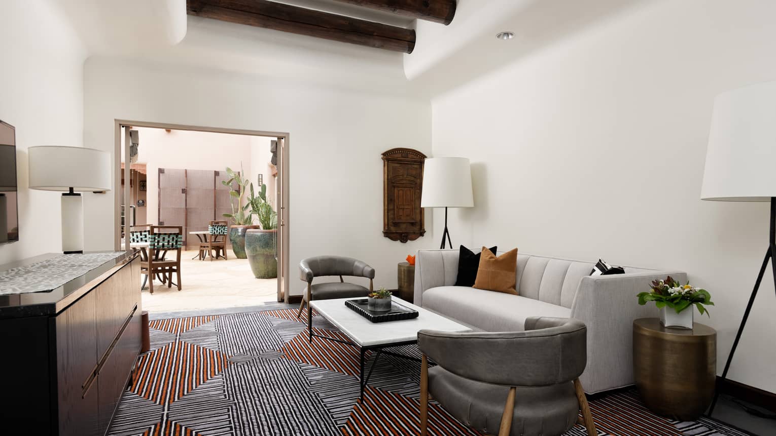 A room with a patterned carpet, couch, two chairs and standing lamps on either side
