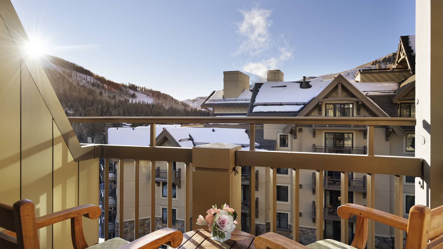 A balcony with two wooden chairs looking at cabin like buildings and a mountain in the distance.