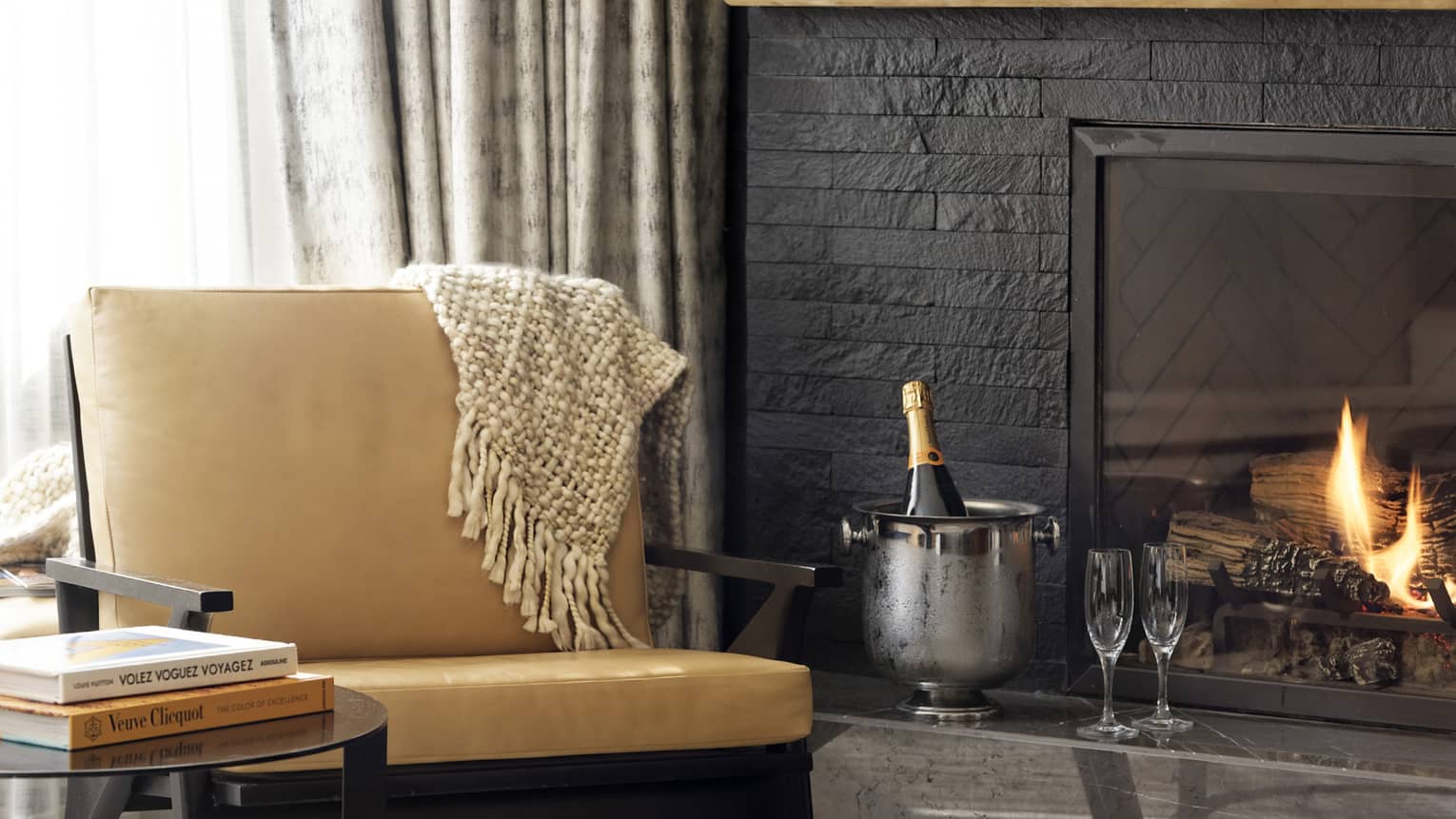 Leather chair, round side table, fireplace, ice bucket with bottle of champagne and two flutes