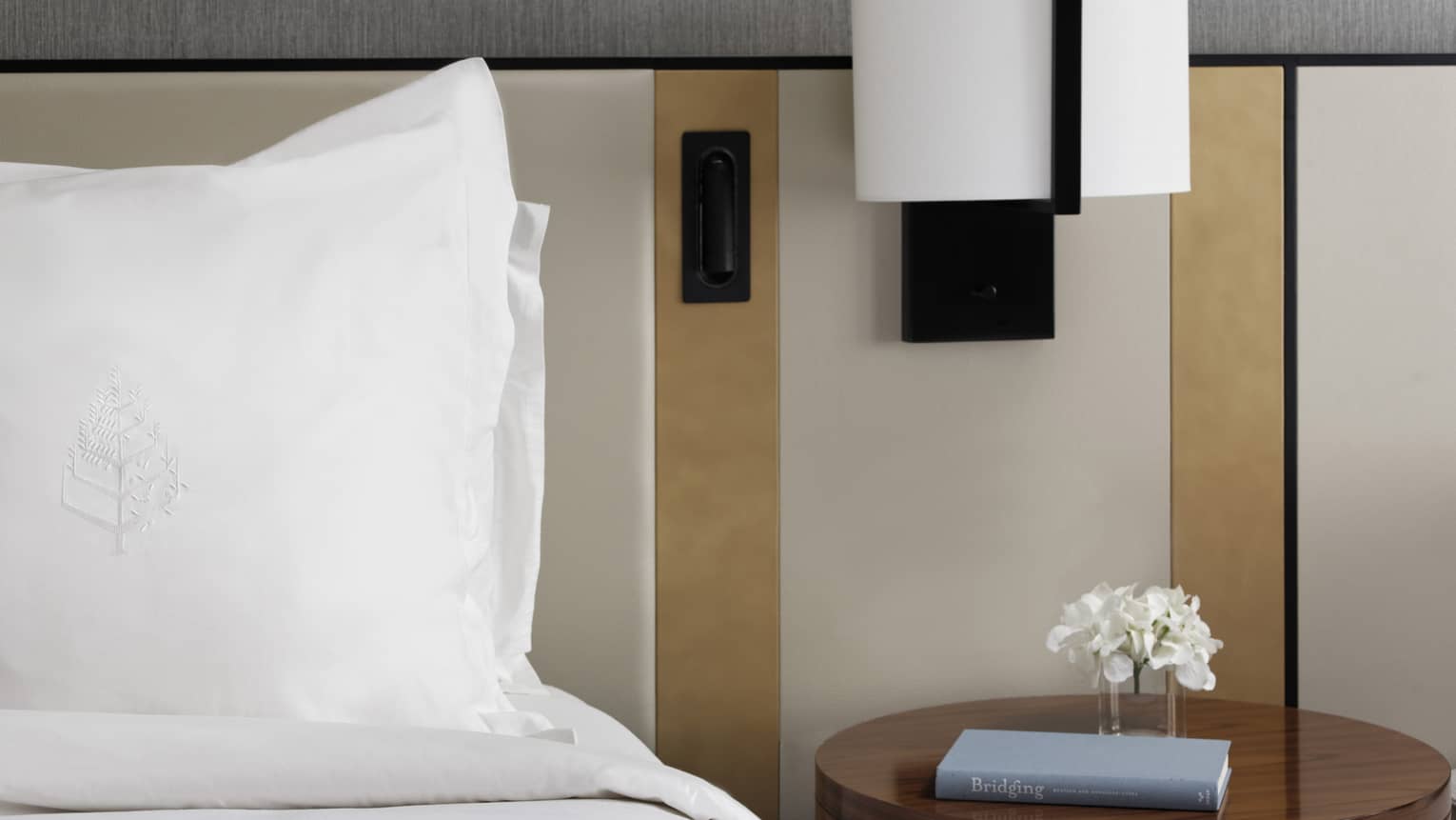 Bed with white linens, round side table with book, reading lamp