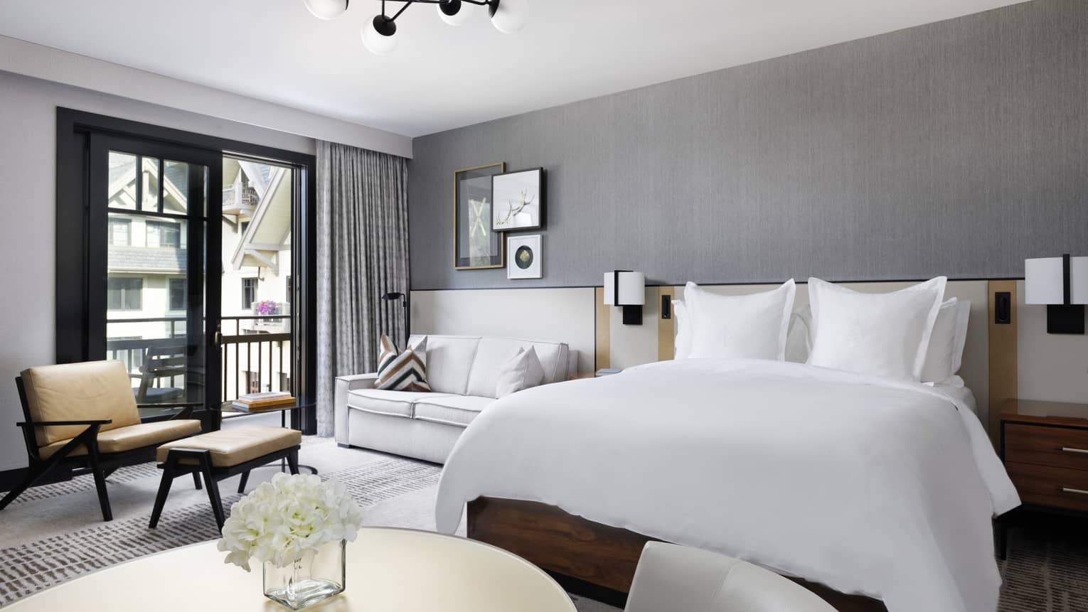 Guest room with King bed, white linens, small round dining table, white leather loveseat, arm chair, glass doors leading to balcony