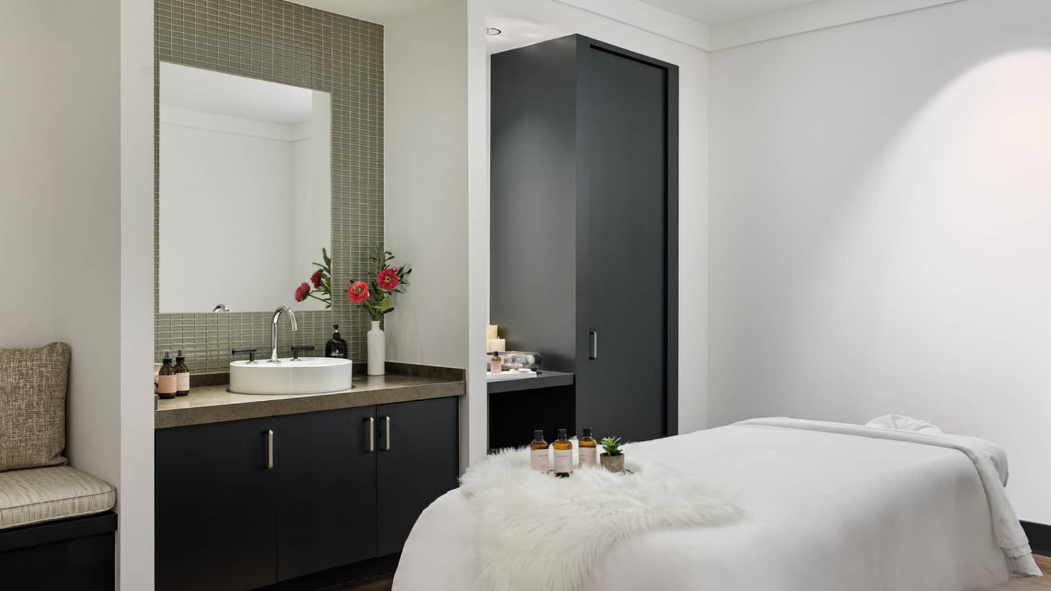 Spa room with massage table, sink with a vase of flowers on it, and cabinets.