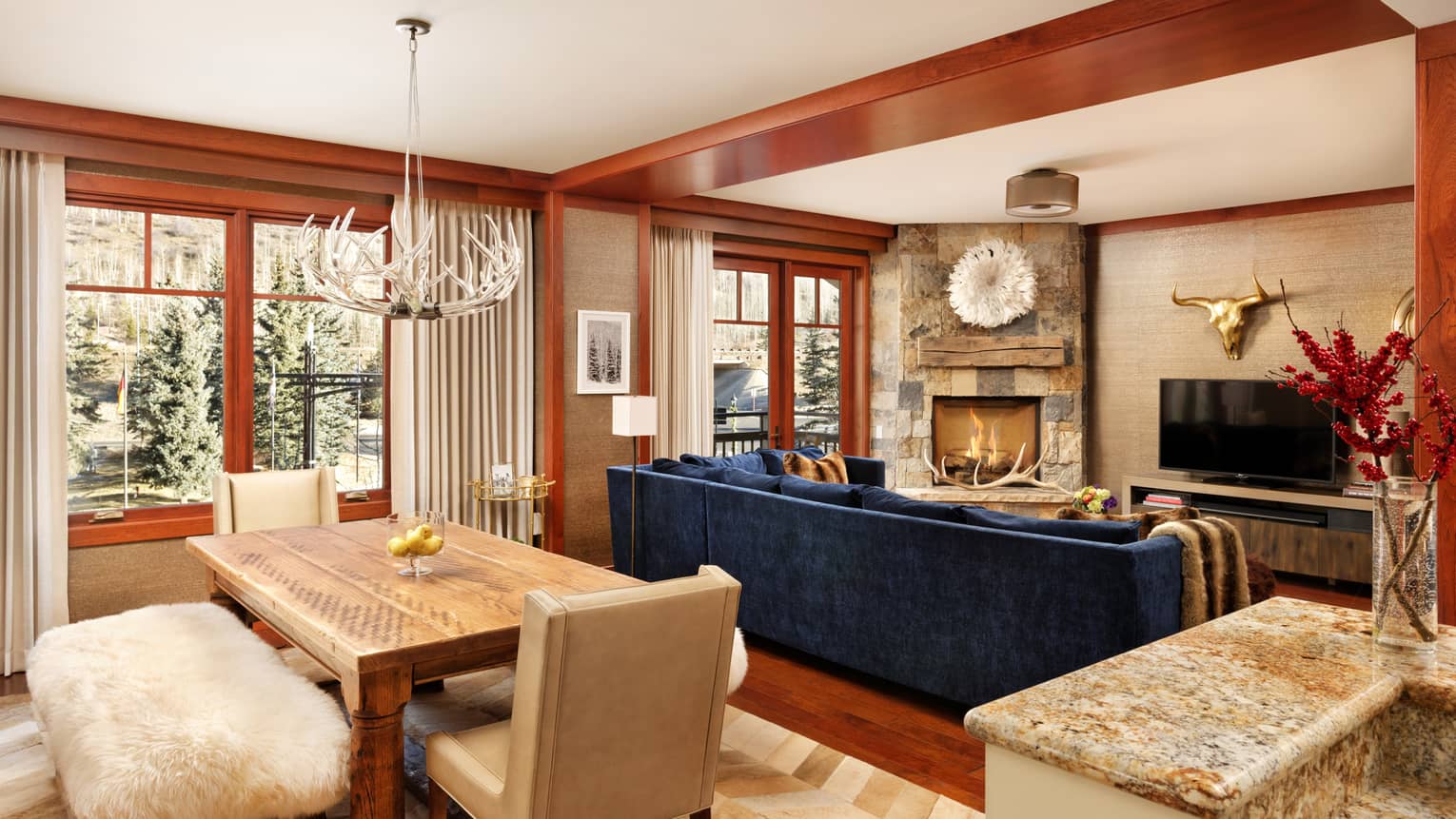 Antler chandelier over  dining table with shag bench near blue sofa, fireplace