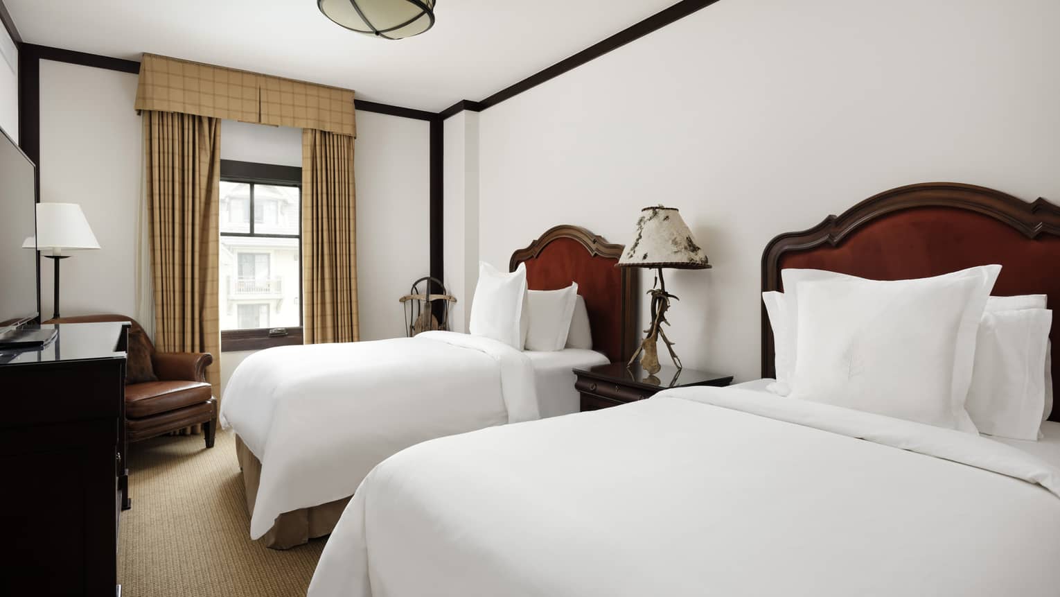 Bedroom with two twin beds, tan curtains and carpet, dark wooden dresser