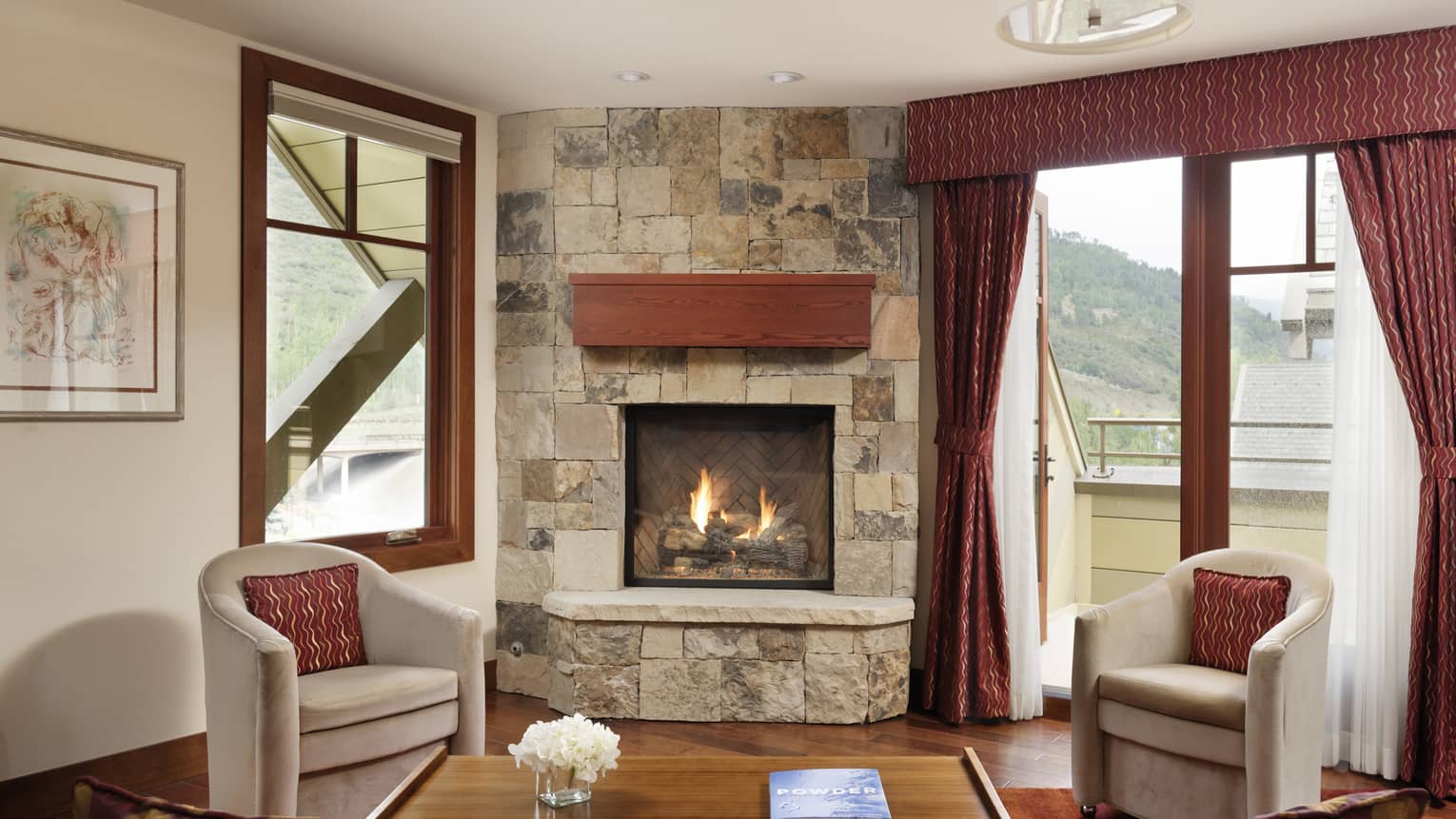 Living area with stone fireplace, two grey chairs, walk-out balcony
