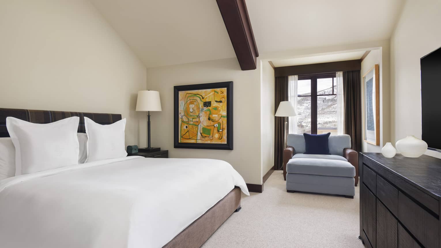 Bedroom with king bed, wooden ceiling beam, blue arm chair and dresser