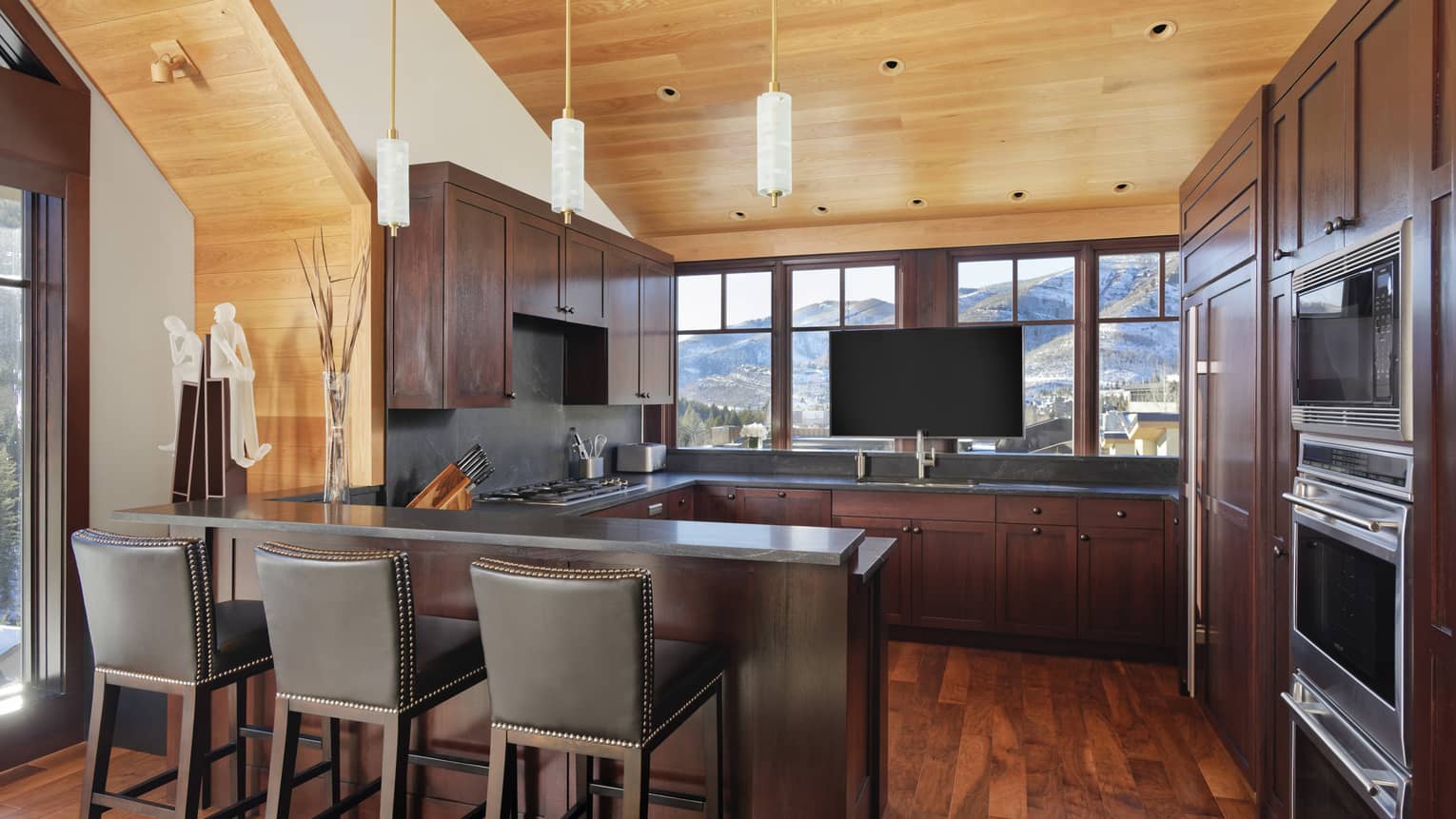 Kitchen with bar counter, three leather bar-height chairs, wooden ceiling