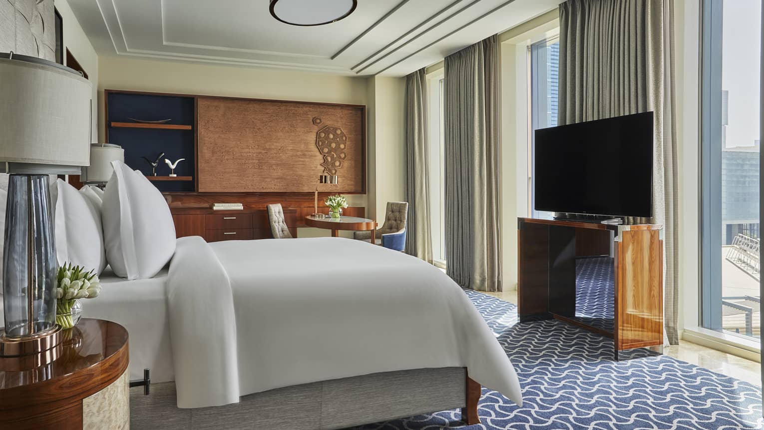 Luxury hotel room with a king-size bed, modern decor, large TV, a seating area and floor-to-ceiling windows with city views