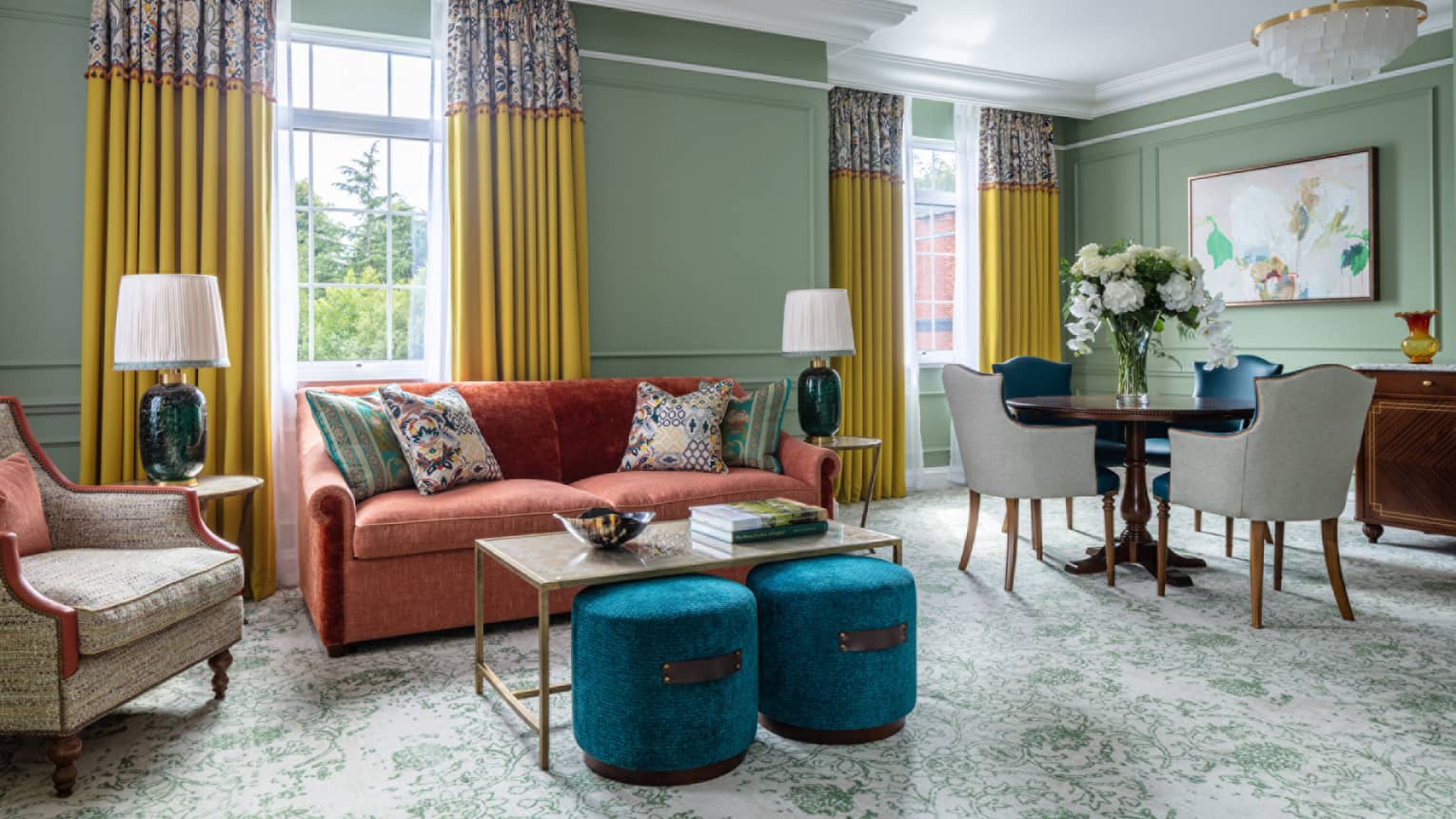 Guest room with red couch, matching coffee table and end tables, round wooden table and four leather chairs, twin windows with yellow drapes