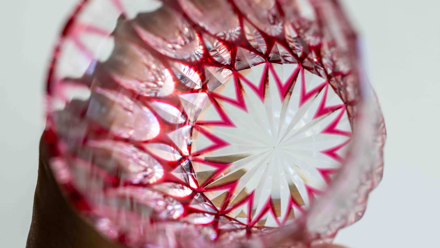 Extreme close-up inside a bright-red cut glass tumbler with a starburst base and intricate geometric patterns on the sides.