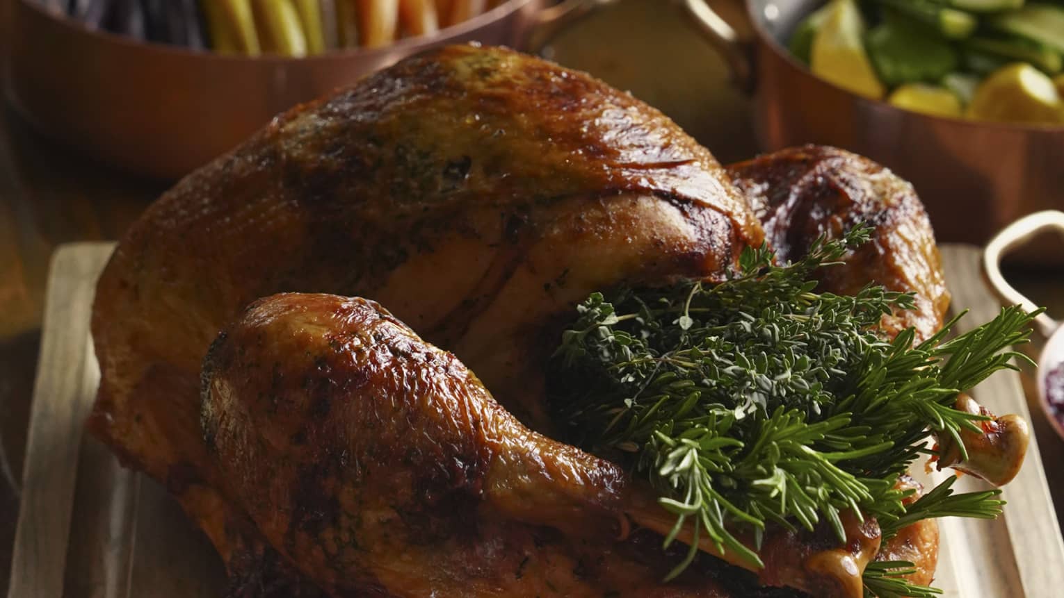 Festive turkey stuffed with rosemary on carving board, accompaniments and side dishes in the background