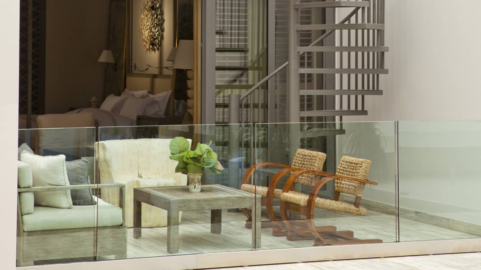 Private villa patio seating area behind glass balcony, bedroom in background, spiral outdoor staircase