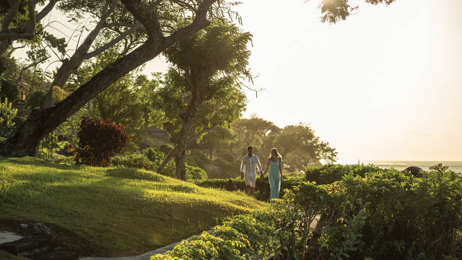 Couple walking hand-in-hand along pathway through beachfront garden