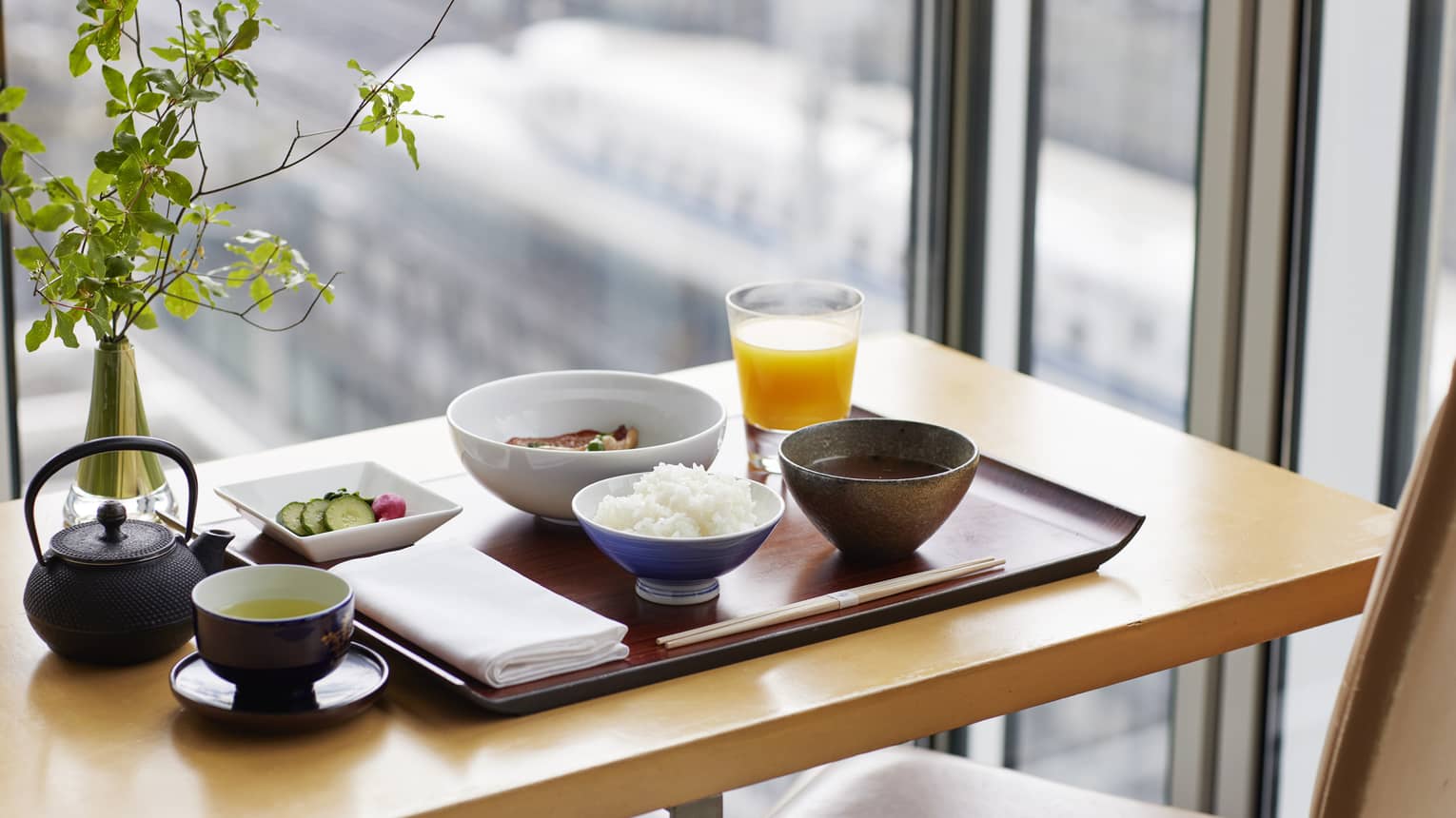 Japanese Breakfast on wooden tray with plant, window overlooking bullet trains
