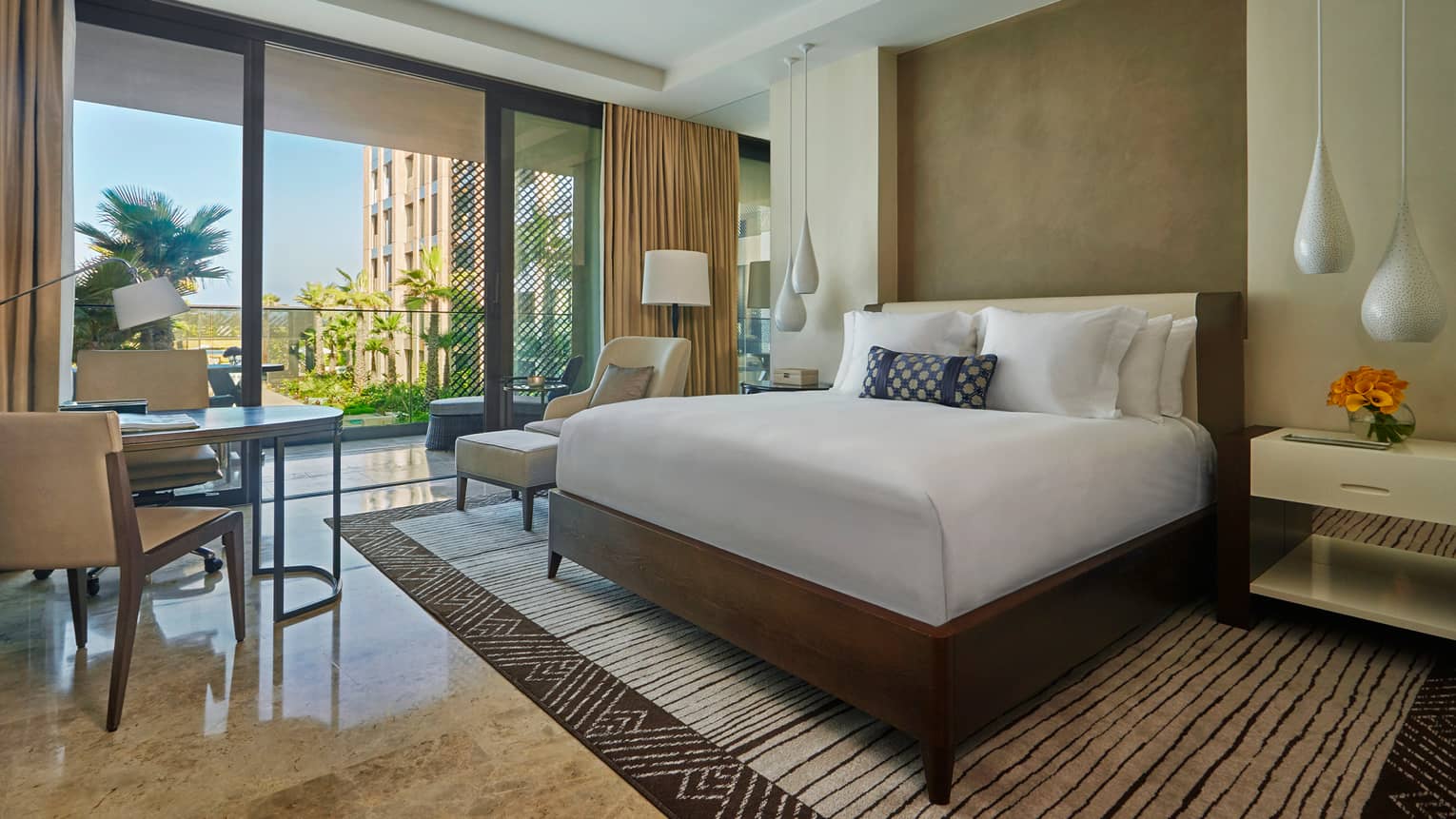 Deluxe Room hotel bed, white teardrop hanging lamps, tables by patio doors