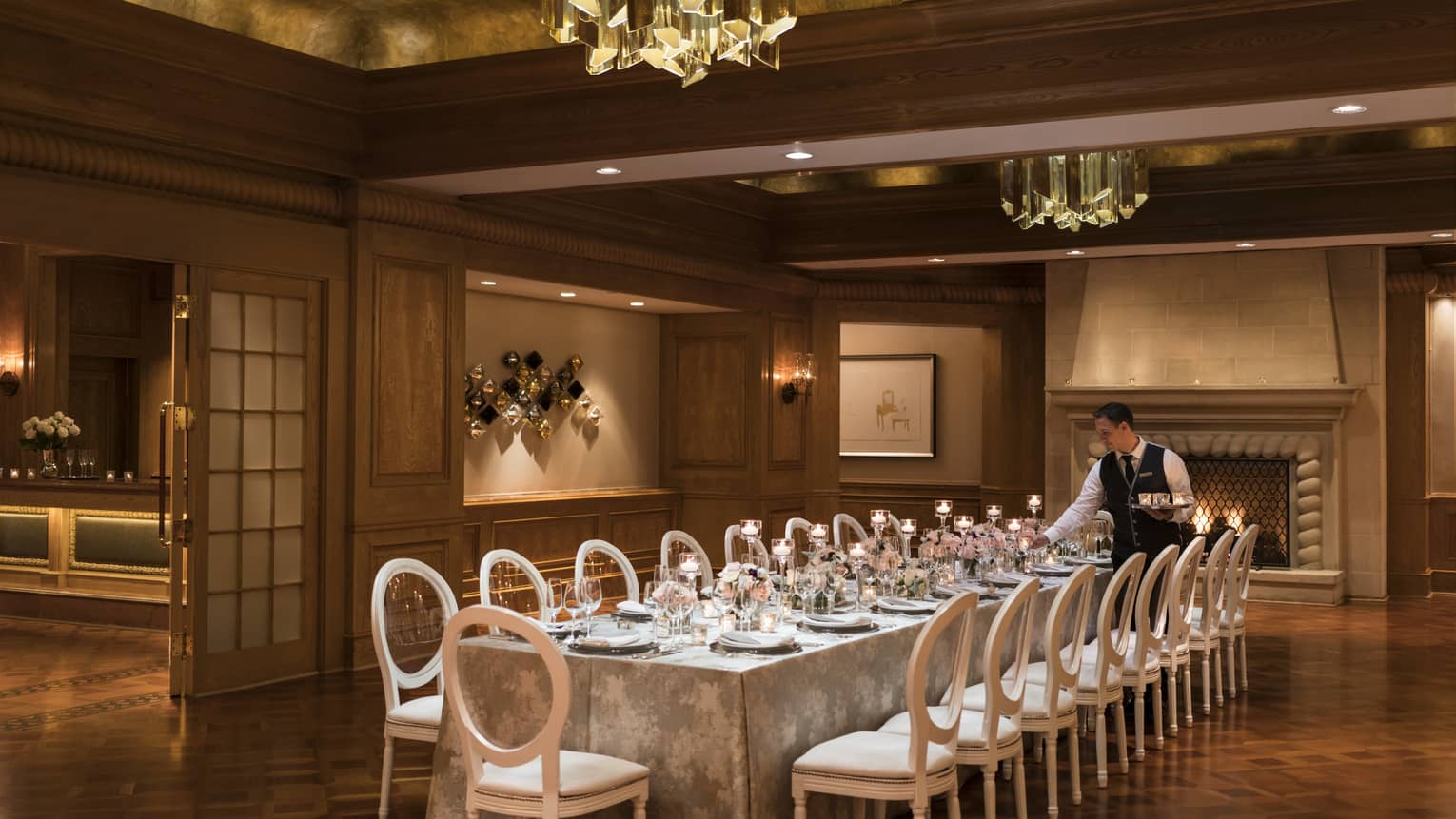 Four Seasons wedding staff places glowing candle on long dining table in banquet room