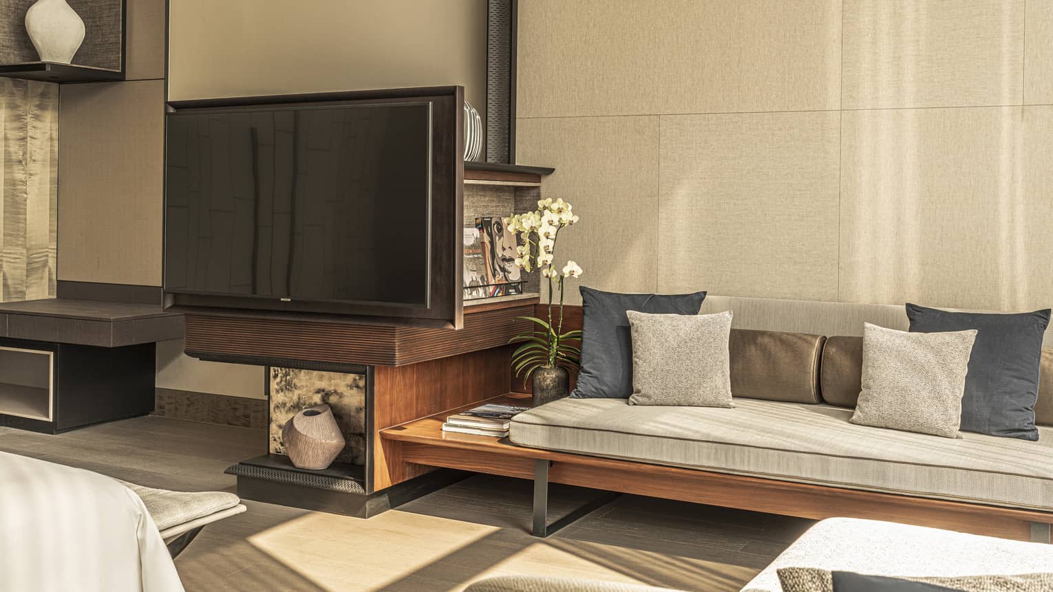 Wood and cushioned sofa next to a TV in a hotel room