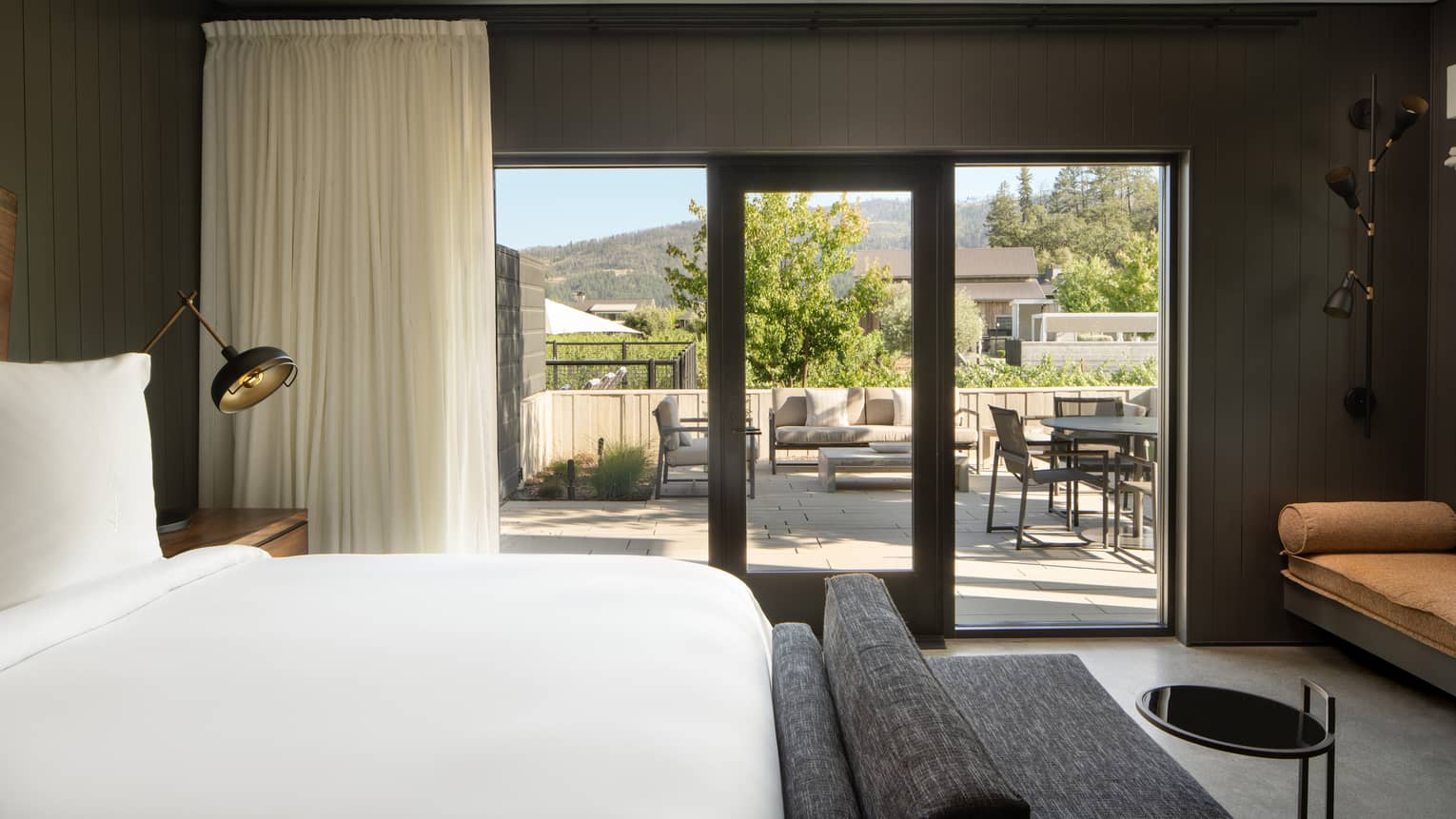 Bedroom with king bed, dark grey chaise and walk-out terrace