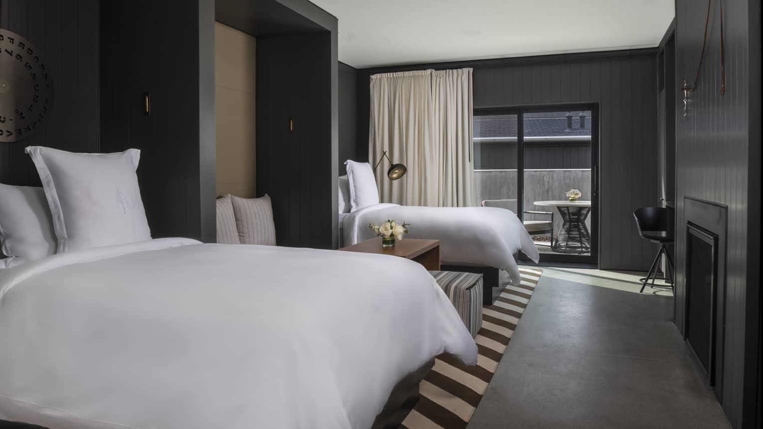 Luxury villa bedroom with two beds, dark walls, modern decor and sliding glass doors leading to a private patio with outdoor seating