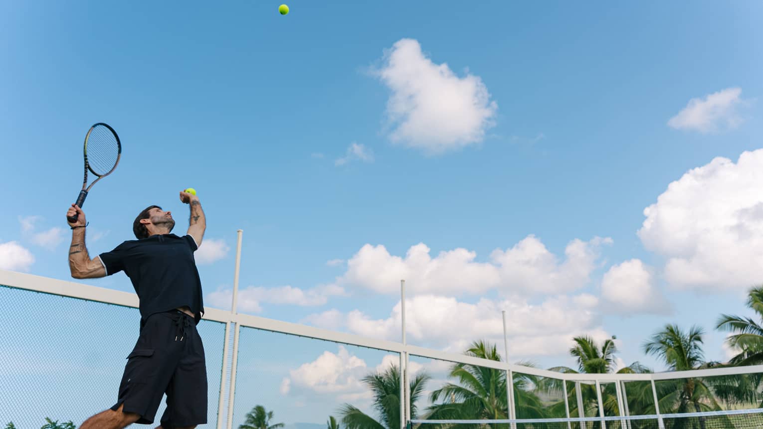 A man throws a tennis ball in the air, getting ready to serve