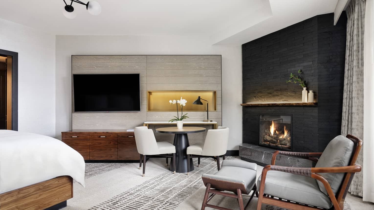 Large bedroom of a hotel suite, featuring a king bed, dining table, arm chair, TV and fireplace