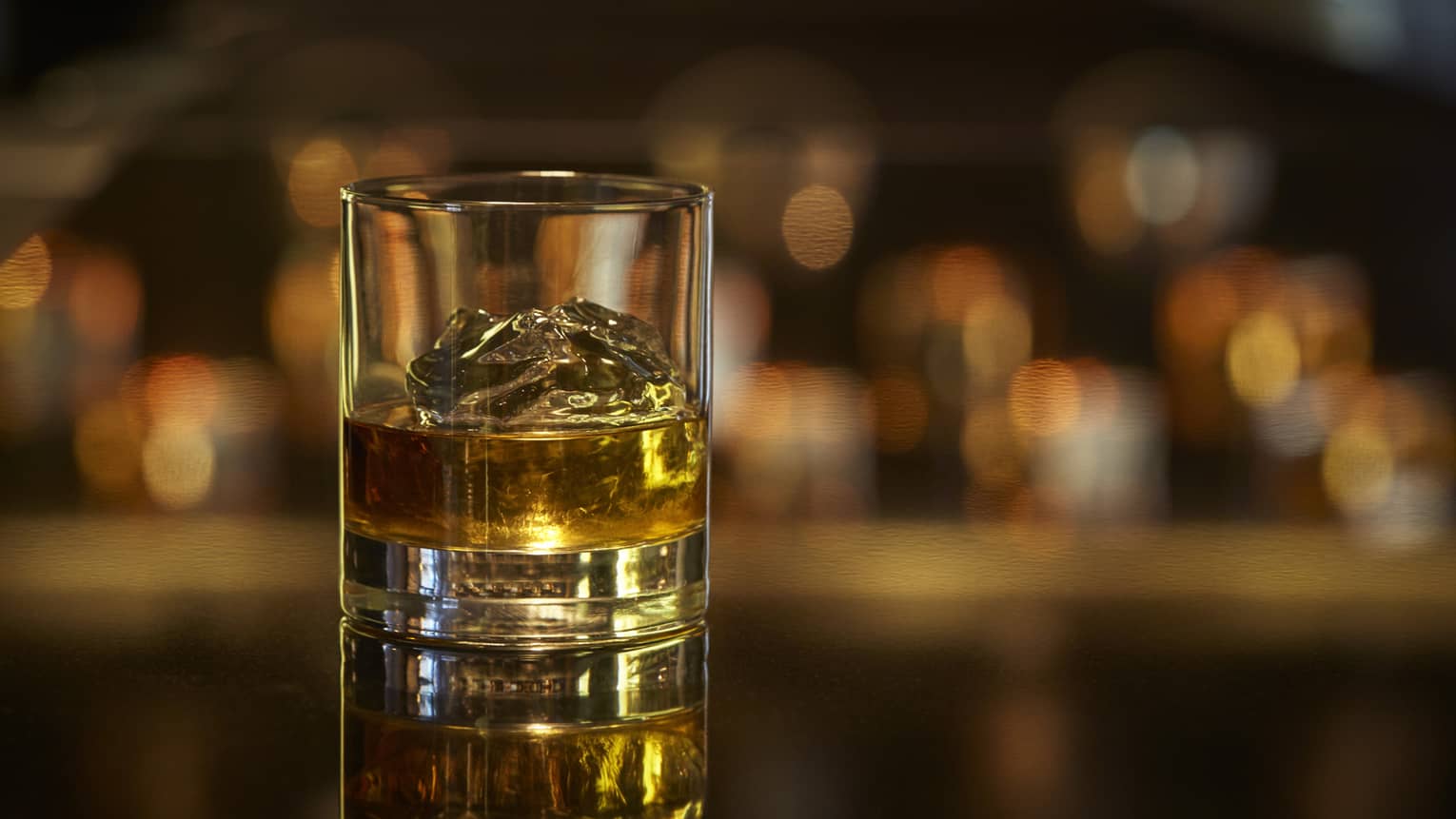 Scotch on the rocks, liquor on ice cubes in rock glass on bar 