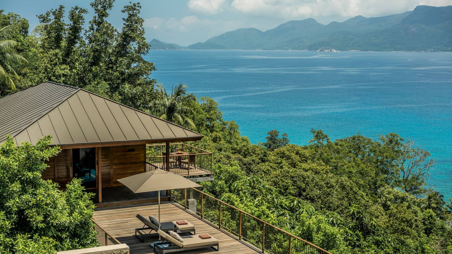 View over wood patio, villa roof on green mountain slope, blue ocean in background