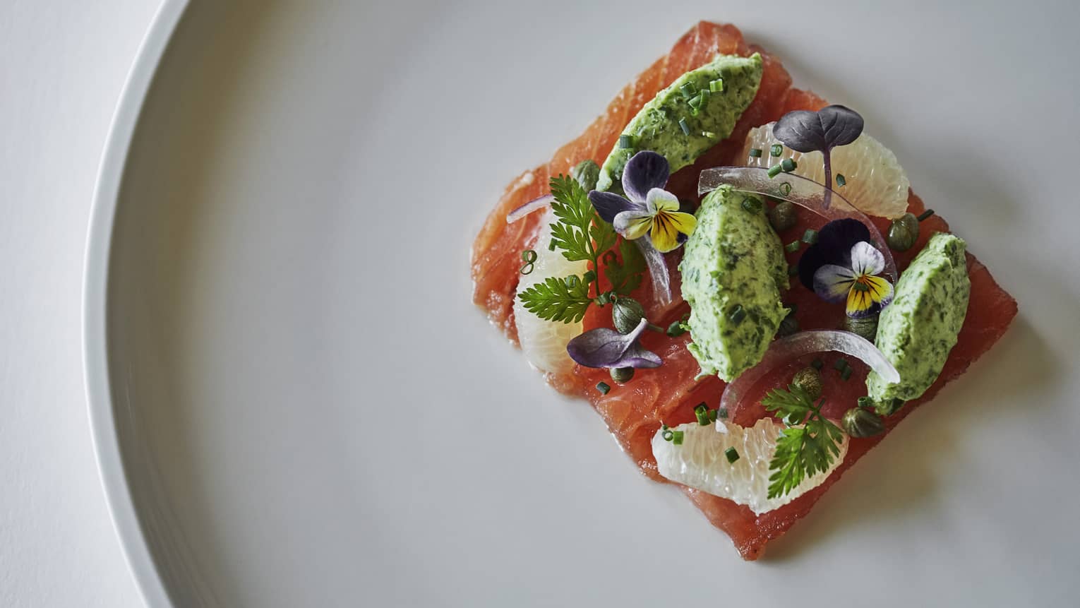 Raw salmon sashimi topped with small fruit, flower garnishes