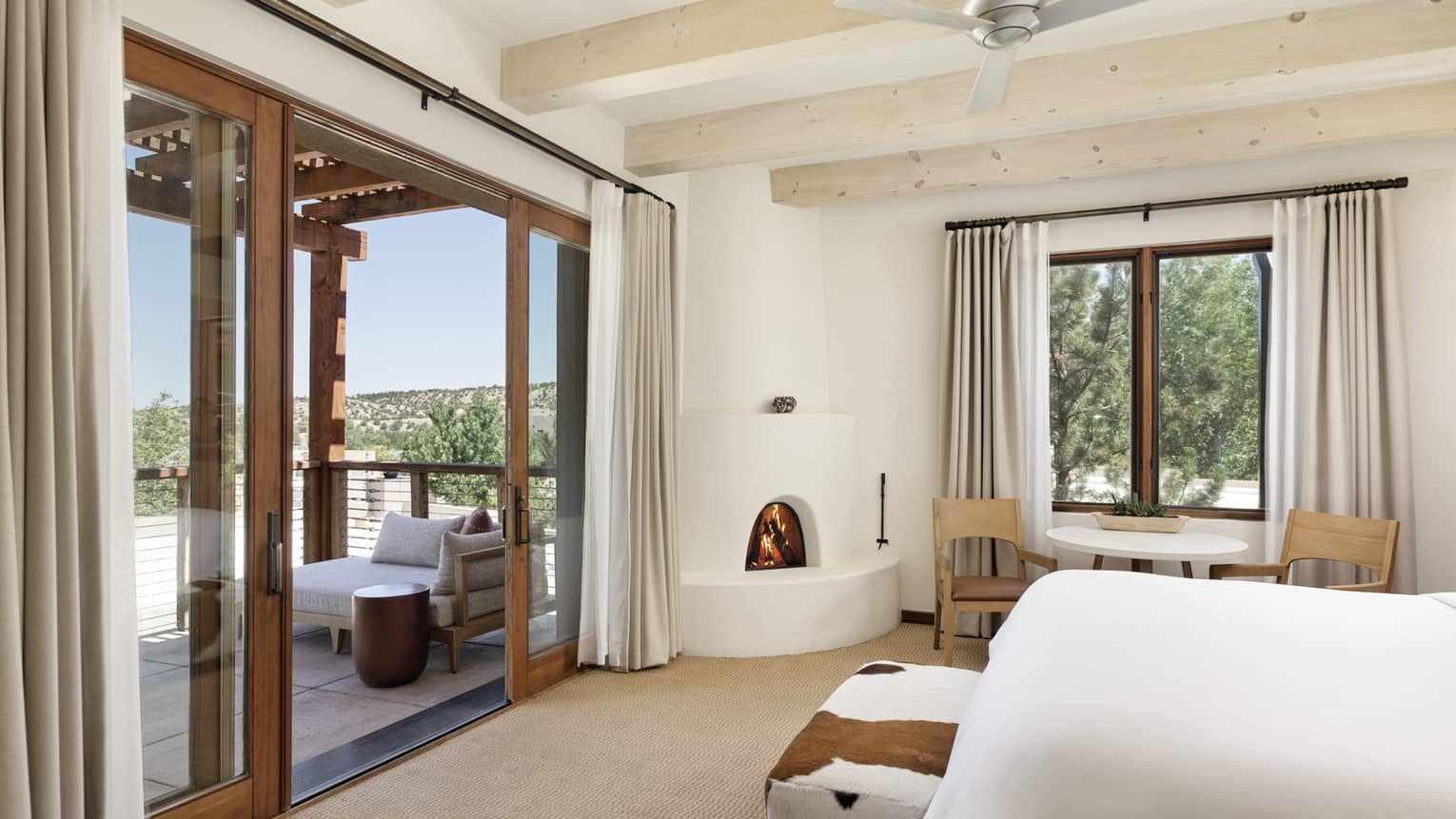 A spacious modern mountain guest room with a fireplace, window seating area and patio overlooking a mountain view