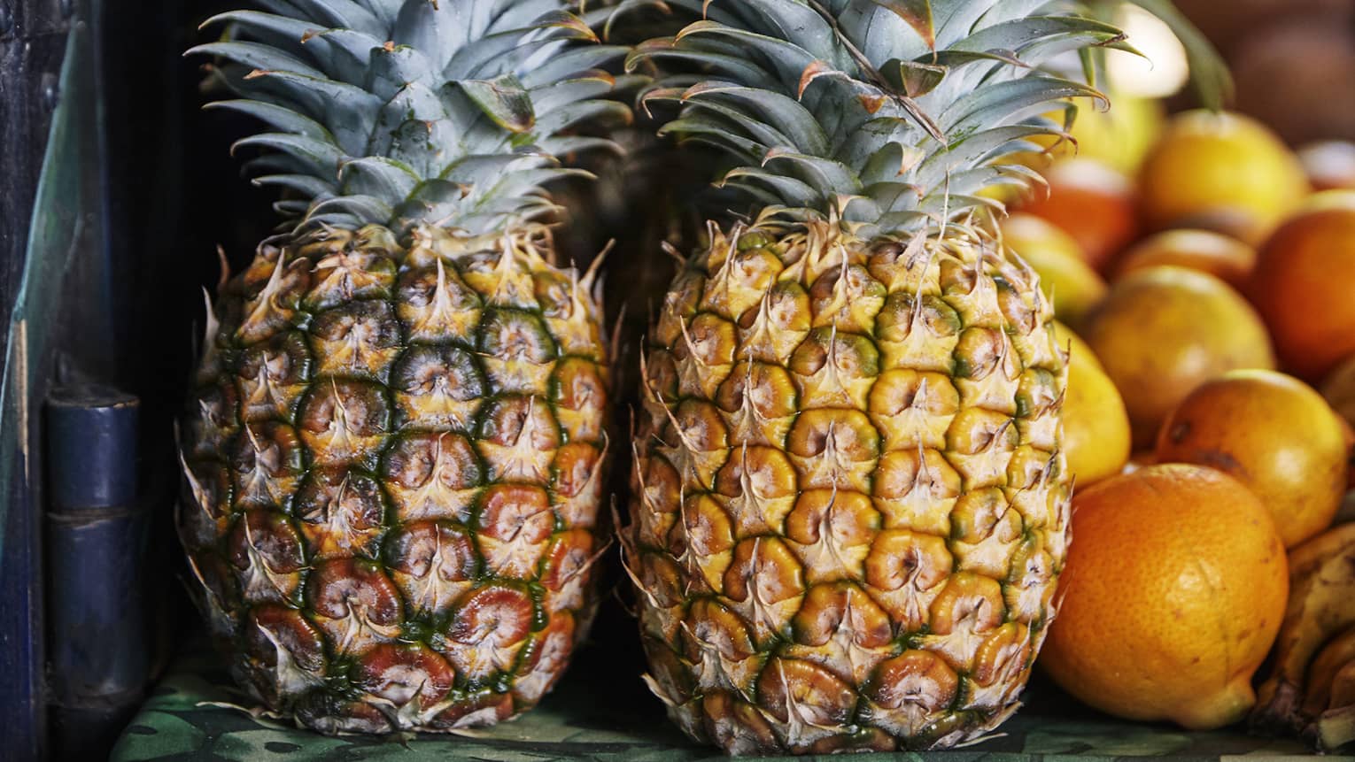 Two whole pineapples next to oranges on table