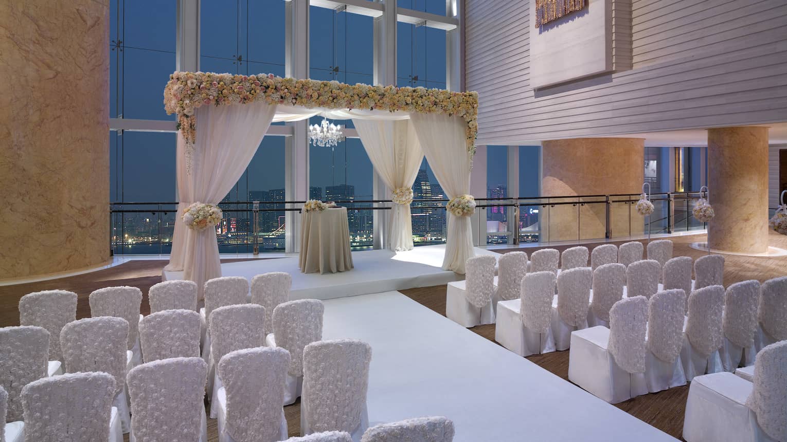 Rows of white chairs face wedding altar under tall loft windows 