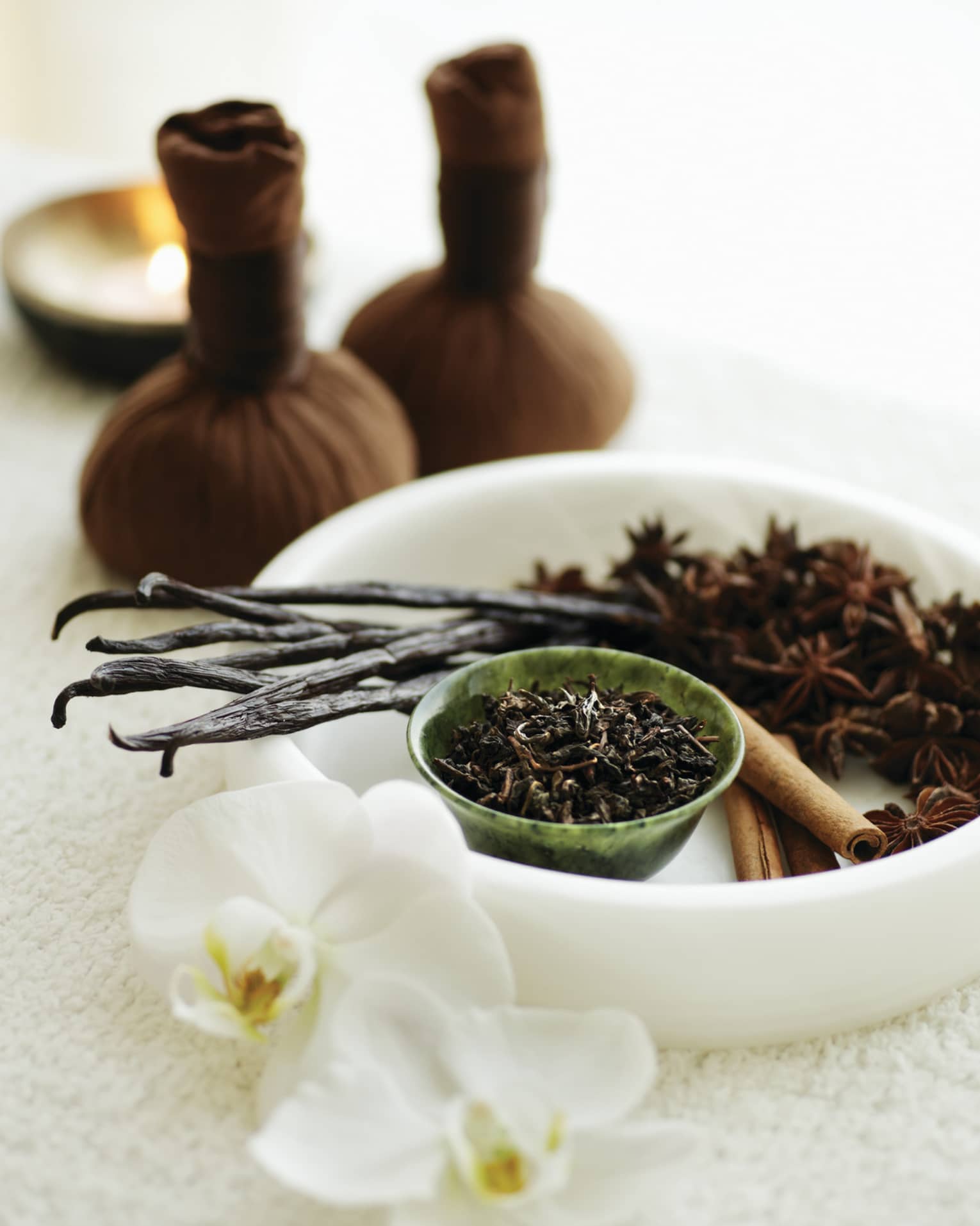 A white bowl filled with various spa ingredients like vanilla bean, star anise and cinnamon sticks