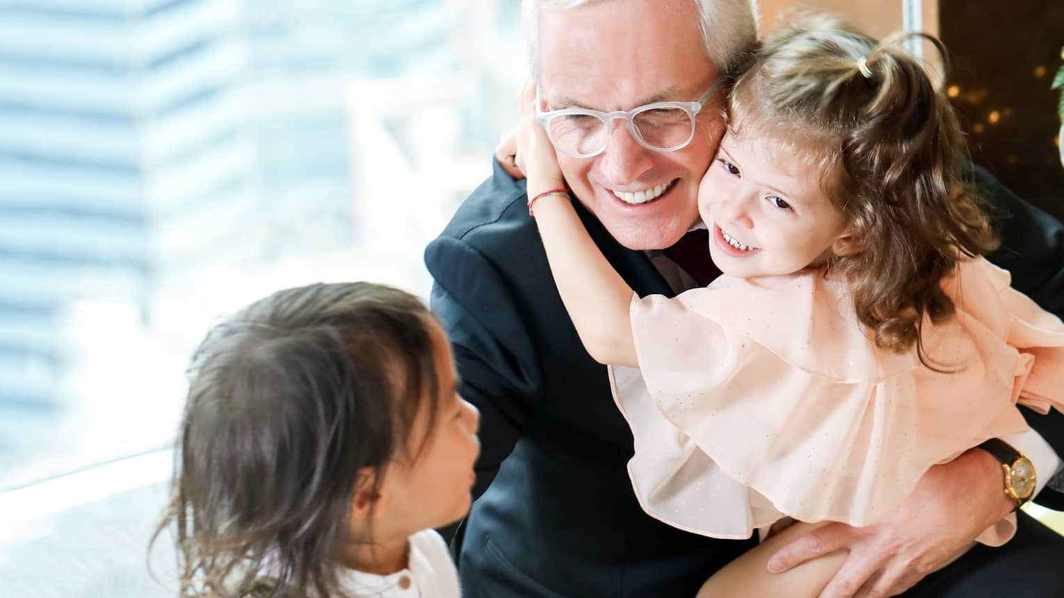 Smiling grandfather with smiling young girl on his knee, arms around his neck, young boy looking on