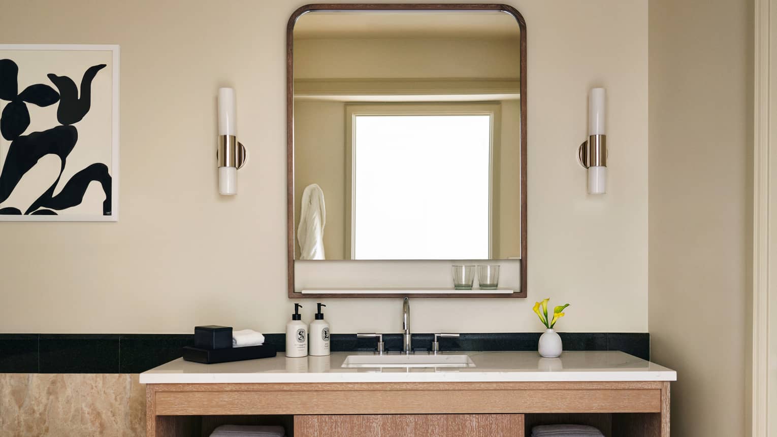 Bathroom with wood and marble vanity, abstract black and white artwork on the wall, mirror and two sconces