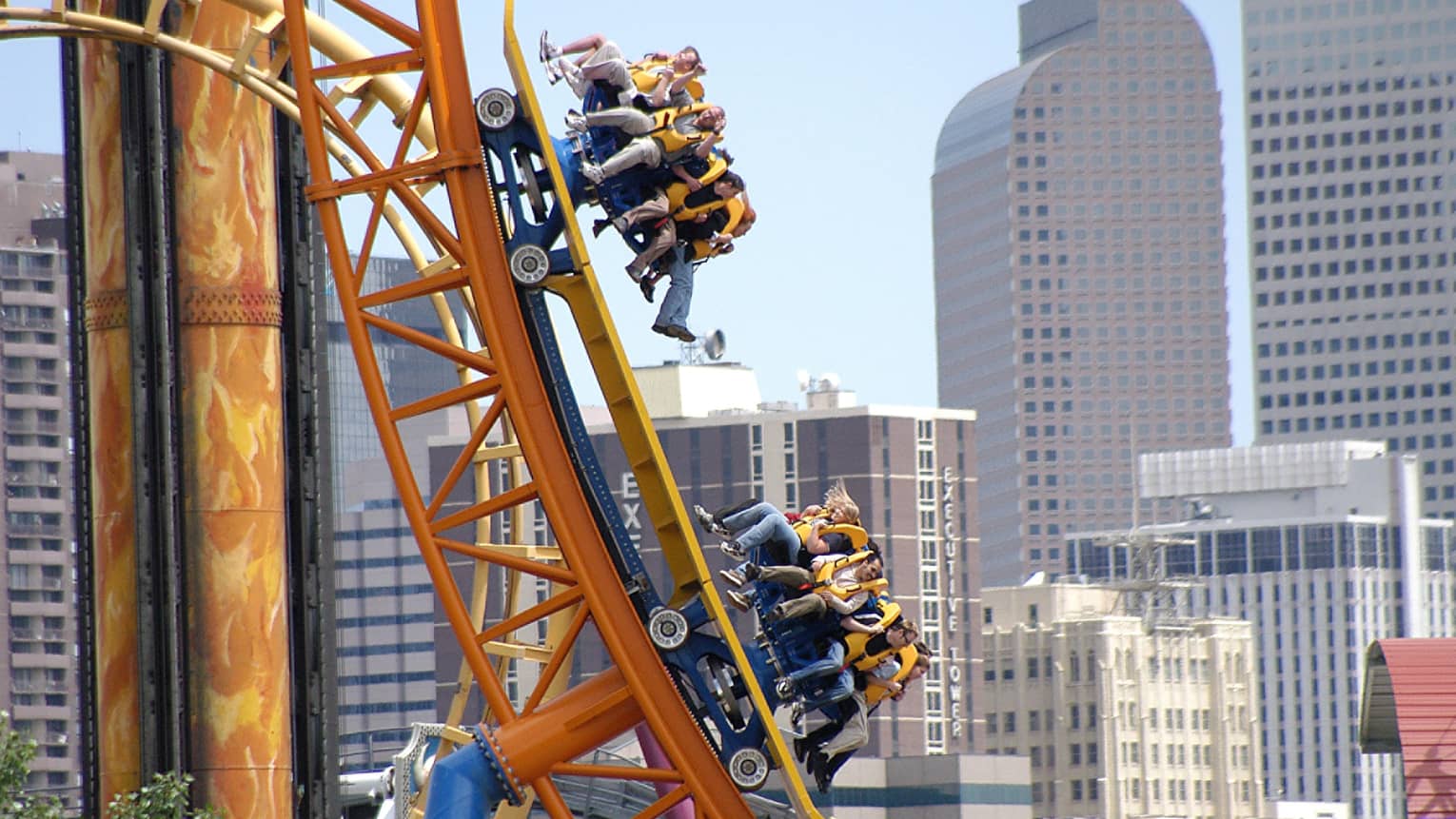 People hang from roller coaster on large orange track at Elitch Gardens Amusement Park