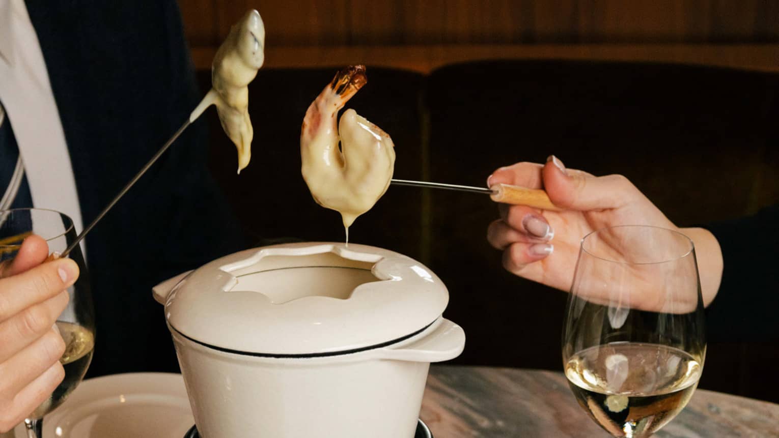 Two people dip shrimp into a white fondue pot