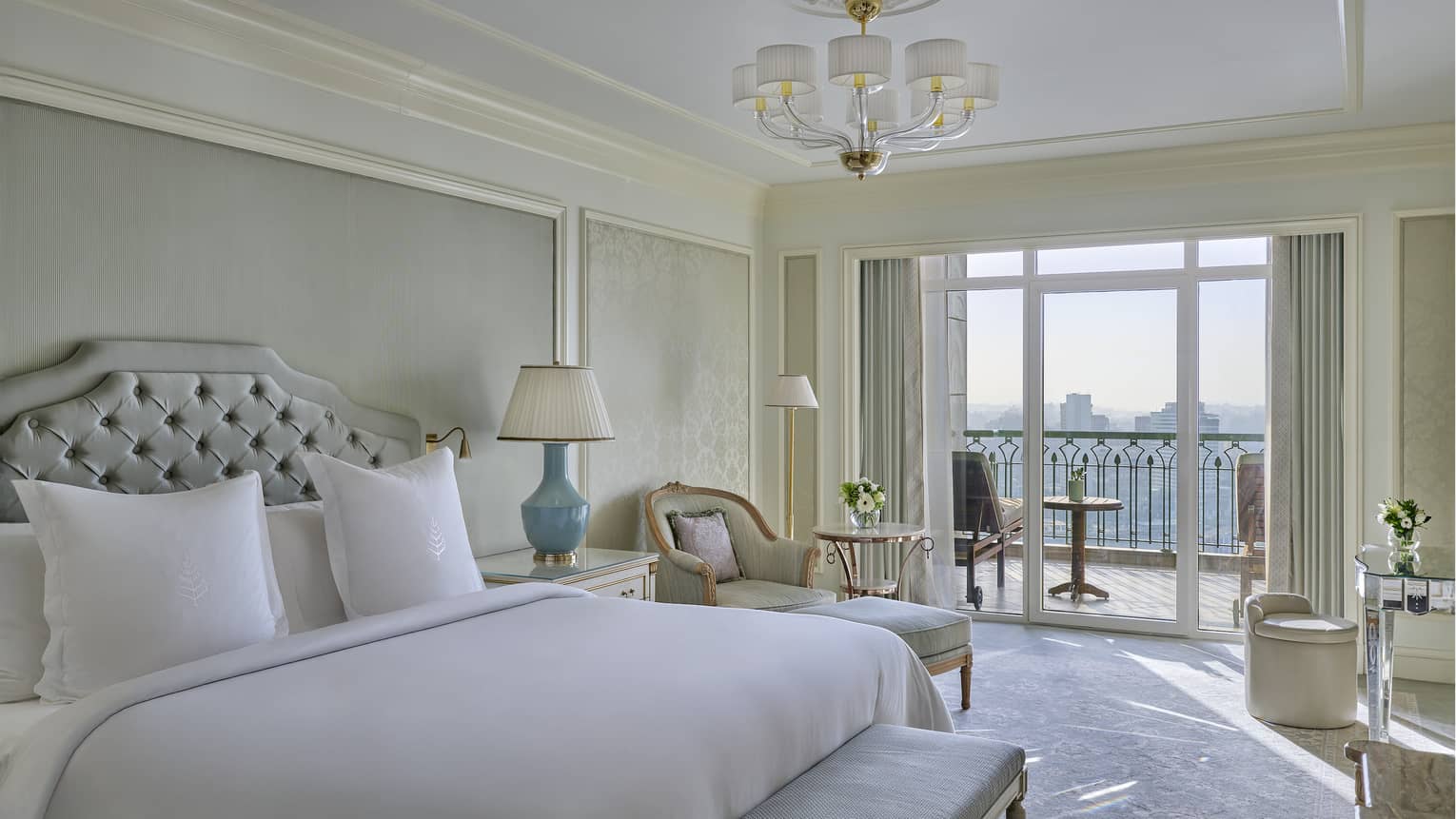Elegant luxury suite featuring white and taupe colours, chandelier, king bed, chaise and walk-out balcony